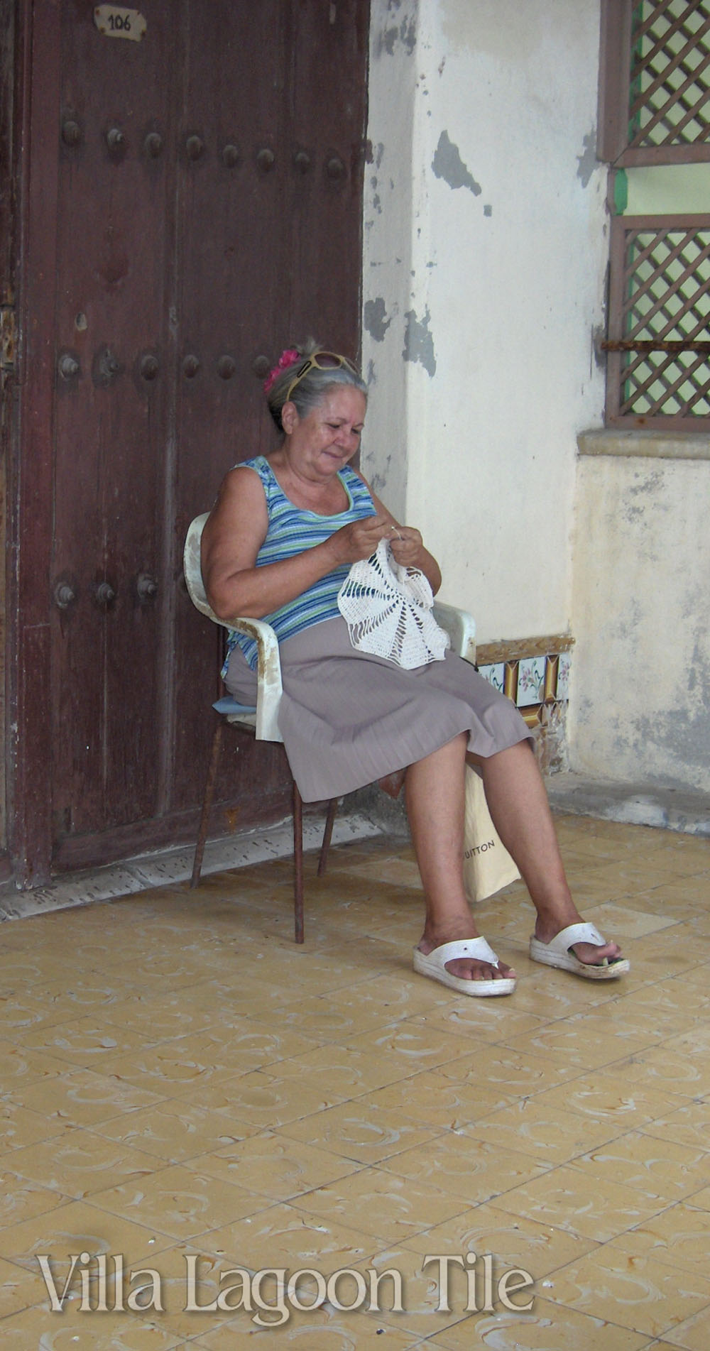 An older Cuban lady crocheting on a cement tile veranda.